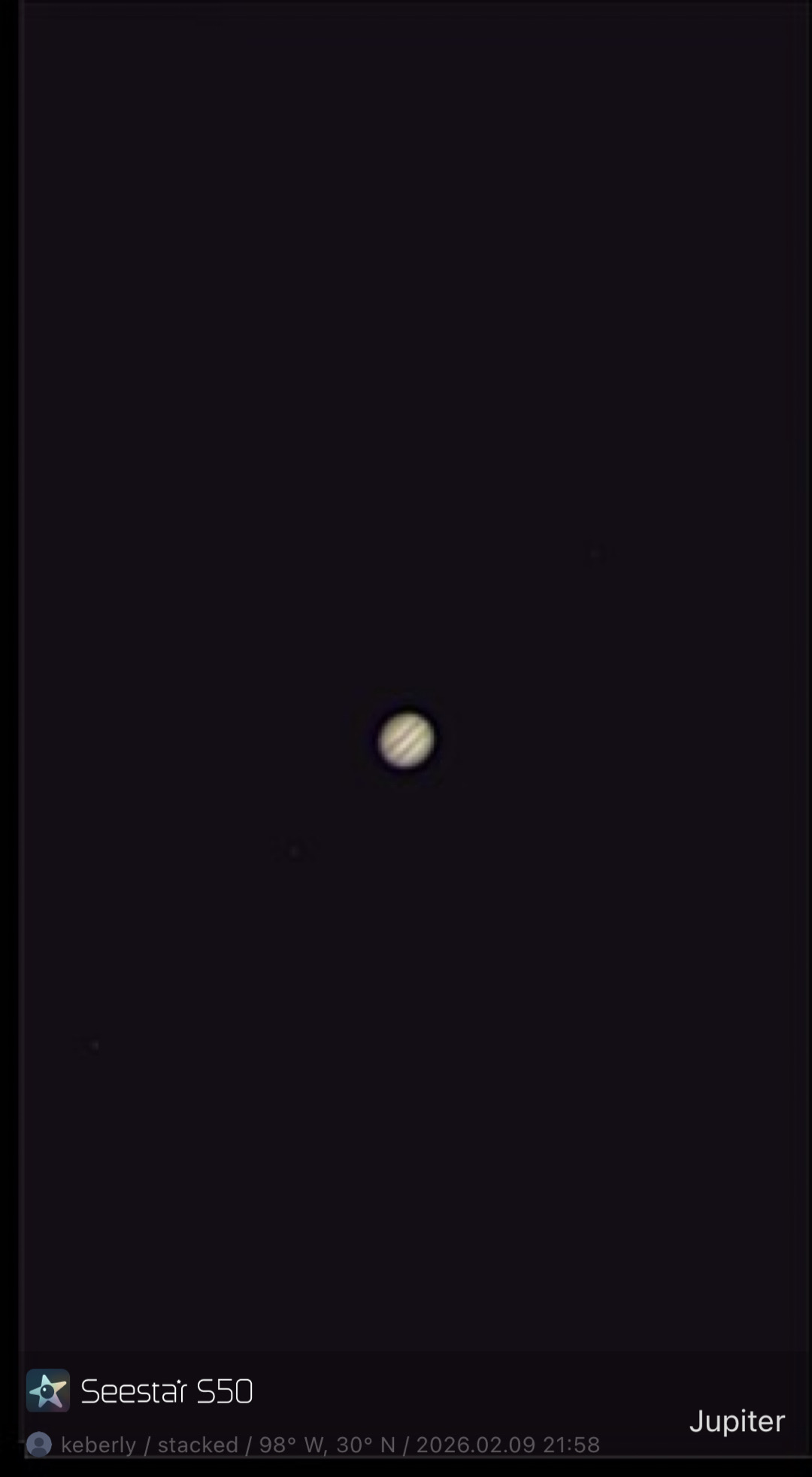 Jupiter photographed from Lakeway, Texas with a ZWO Seestar S50 in Solar System mode — a small tan-and-cream disk with visible parallel equatorial cloud bands, centered in a wide black field.