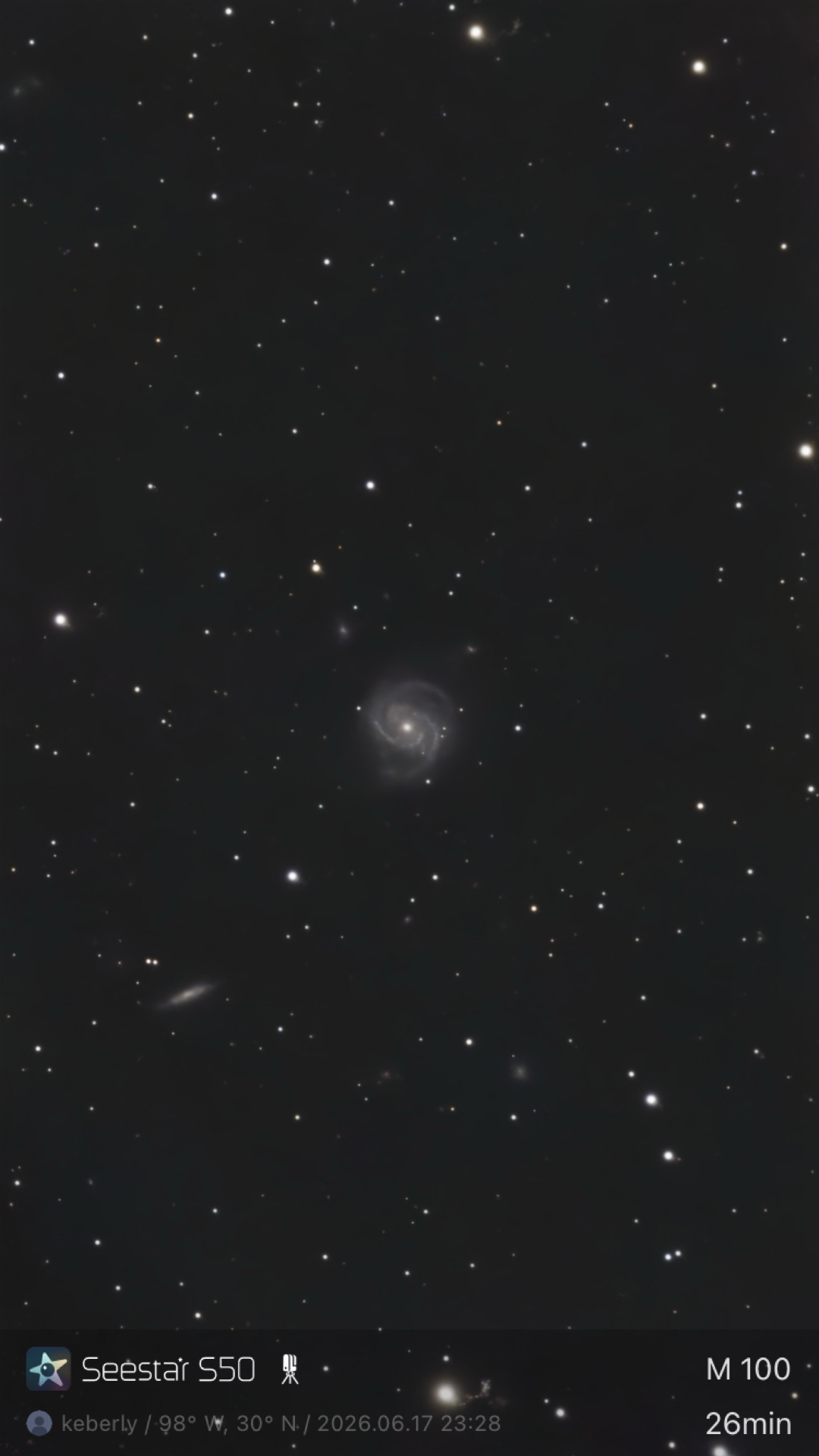 M100 photographed from Bahía de los Ángeles, Baja California with a ZWO Seestar S50 — a face-on spiral galaxy in the center of the frame with resolved arm structure, accompanied by an edge-on companion galaxy in the lower-left and several other faint Virgo Cluster members scattered through the field.
