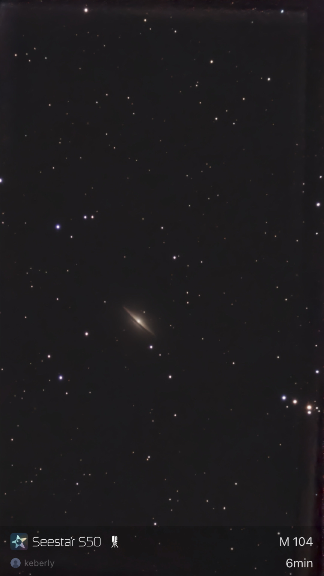 The Sombrero Galaxy (M104) photographed from Lakeway, Texas with a ZWO Seestar S50 — a small but unmistakable edge-on spiral galaxy with a bright central bulge and a dark dust lane cutting horizontally across it, set in a wide starfield.