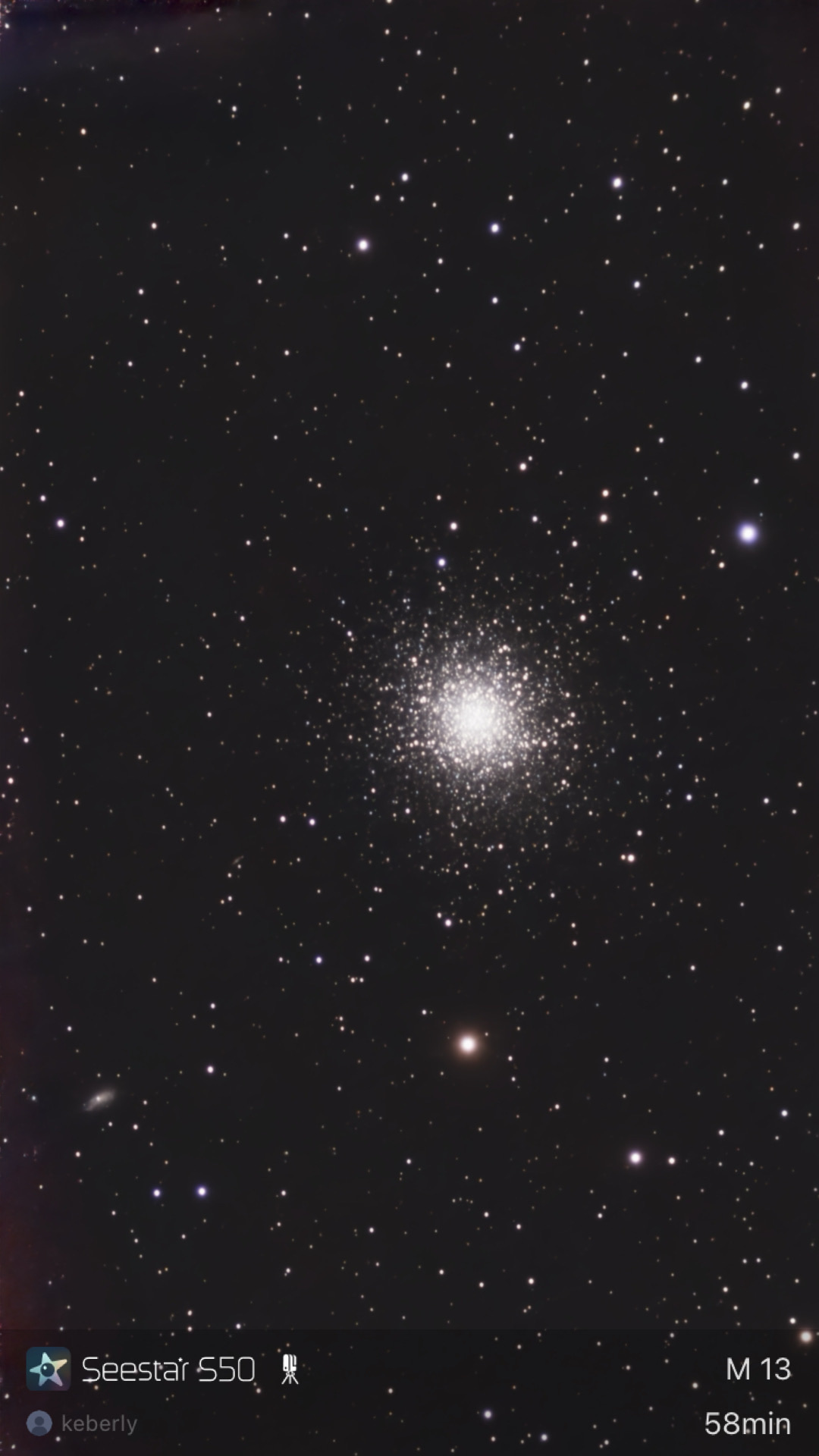 The Hercules Globular Cluster (M13) photographed from Lakeway, Texas with a ZWO Seestar S50 — a dense, resolved ball of hundreds of thousands of stars with a faint background galaxy (NGC 6207) visible in the lower-left corner.