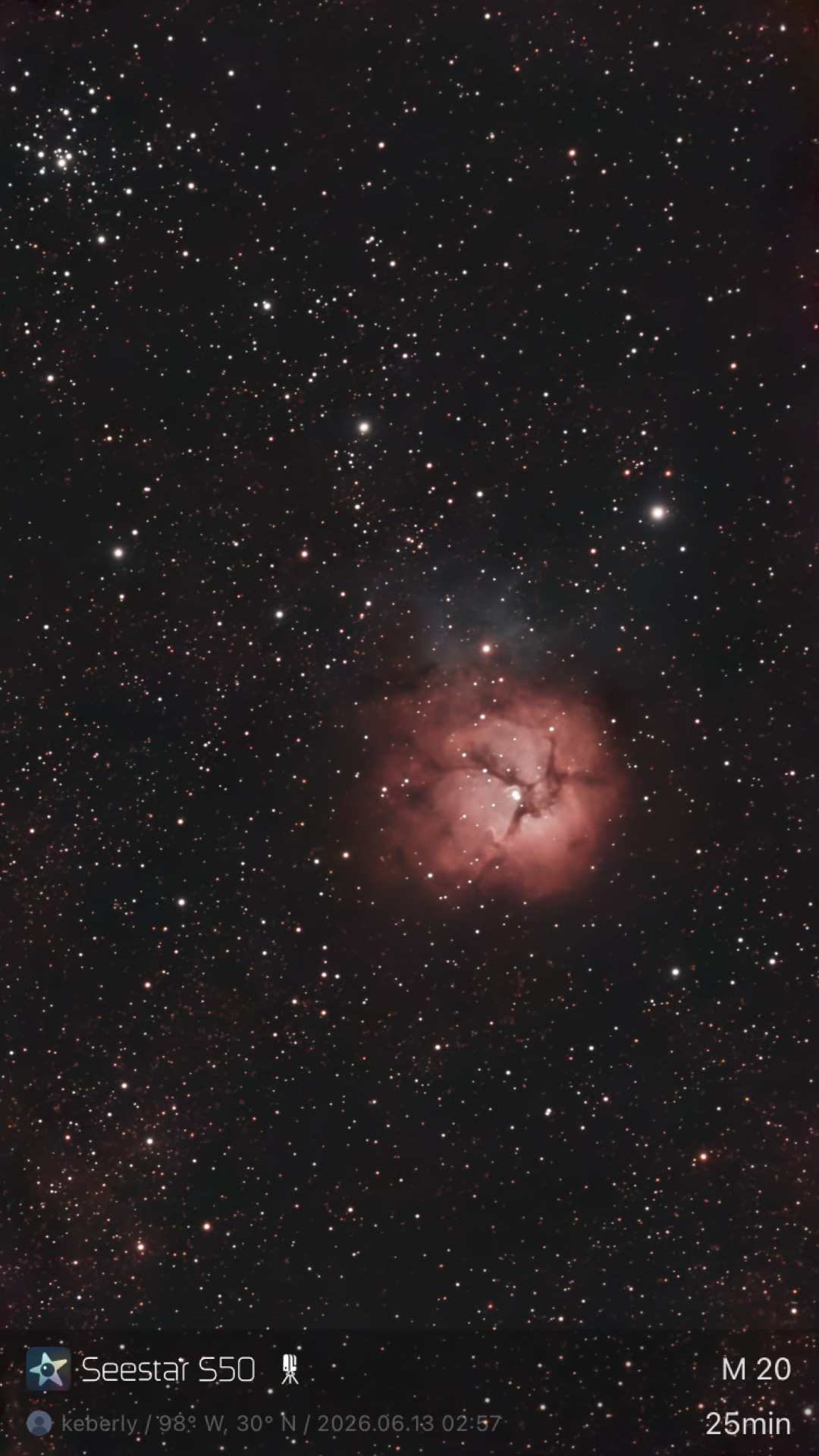The Trifid Nebula (M20) photographed from Lakeway, Texas with a ZWO Seestar S50 — a small pink emission nebula divided into three lobes by dark dust lanes, with a bright young star at its center.