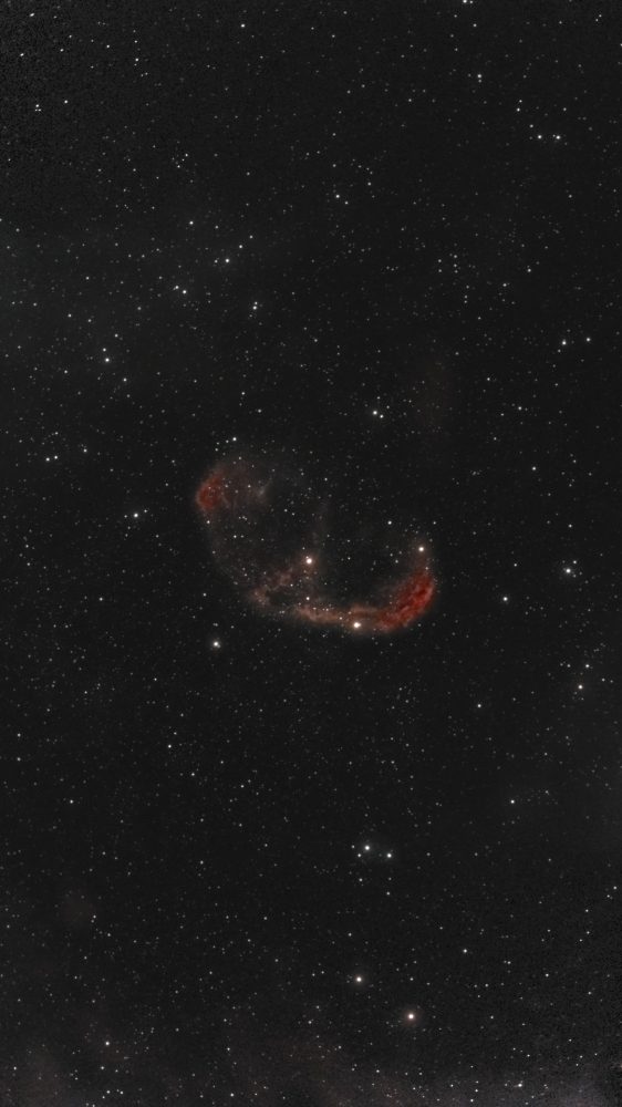 Full-frame view: The Crescent Nebula (NGC 6888) photographed from Lakeway, Texas with a ZWO Seestar S50 — a red-rimmed crescent-shaped shell of gas with mottled interior filaments, floating in a dense Cygnus star field with the central Wolf-Rayet star visible.