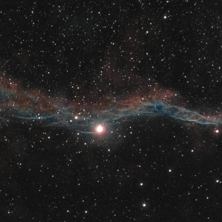 The Witch's Broom (NGC 6960, Western Veil) photographed from Lakeway, Texas with a ZWO Seestar S50 — a braided blue-white filament shaft running through the bright star 52 Cygni, with red nebulosity flanking it.