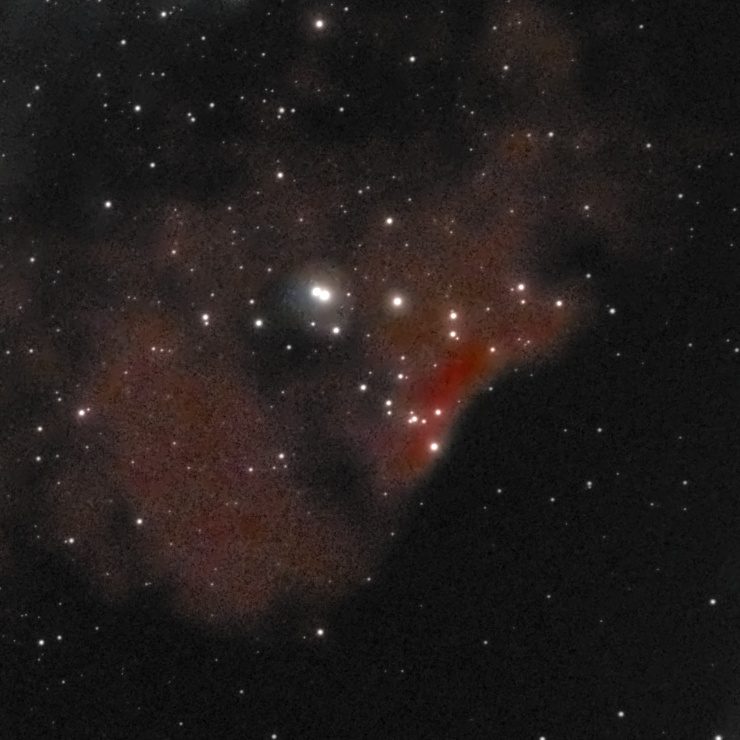 Sh2-140 photographed from Lakeway, Texas with a ZWO Seestar S50 — a compact red ionization rim glowing along the edge of a dark molecular cloud, with a small blue reflection patch and embedded stars.