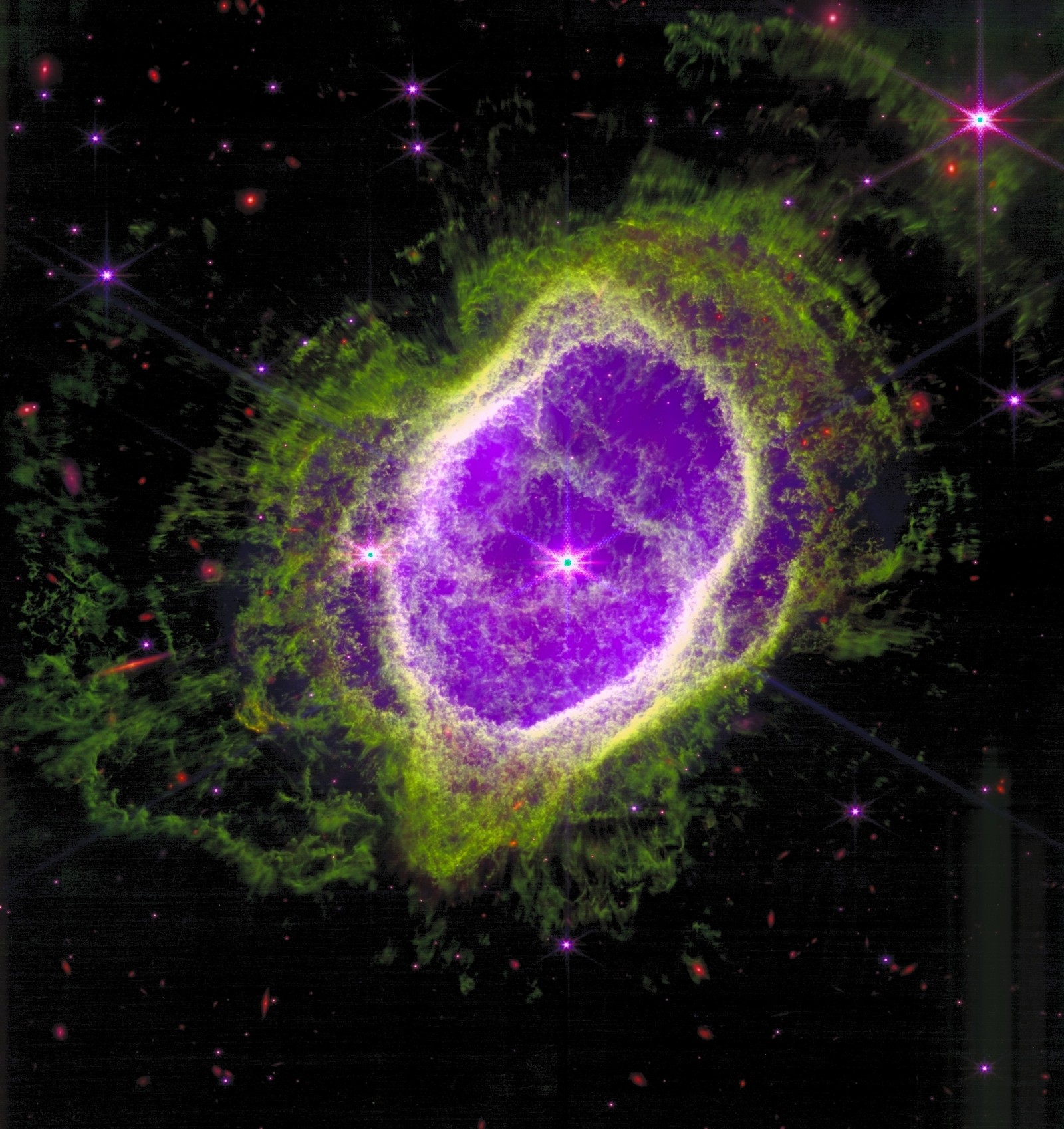 The Southern Ring Nebula (NGC 3132) — a JWST NIRCam image reprocessed by Kyle Eberly. A glowing oval shell of green and gold gas surrounds a purple interior, with two stars at the center, against a black sky dotted with background galaxies.