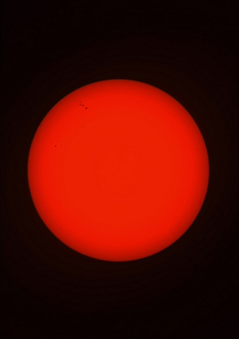 The Sun photographed in white light through a solar filter from Lakeway, Texas with a ZWO Seestar S50 — a deep orange disk with two visible sunspot groups in the upper-left quadrant.