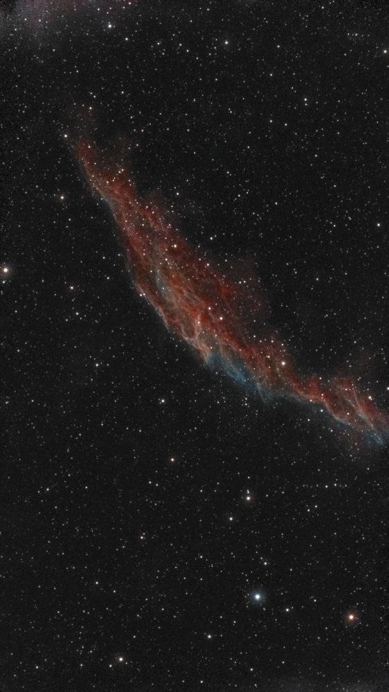 Full-frame view: The Eastern Veil Nebula (NGC 6992) photographed from Lakeway, Texas with a ZWO Seestar S50 — braided filaments of red hydrogen and teal oxygen forming a luminous arc across a dense Cygnus star field.