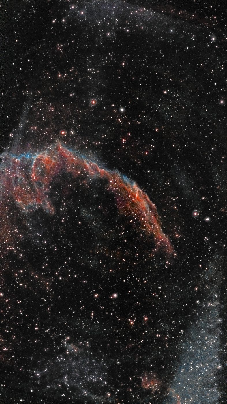 The Eastern Veil Nebula photographed with a ZWO Seestar S50 Pro on its first night of use — braided red and blue supernova filaments in a wide 4K star field, with faint wisps of other sections of the Cygnus Loop visible toward the frame edges.