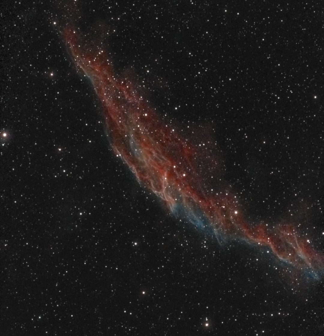 The Eastern Veil Nebula (NGC 6992) photographed from Lakeway, Texas with a ZWO Seestar S50 — braided filaments of red hydrogen and teal oxygen forming a luminous arc across a dense Cygnus star field.